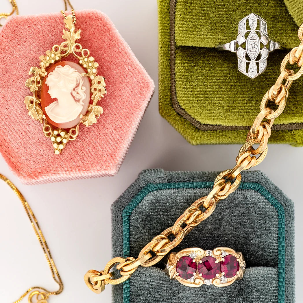 Collection of vintage jewellery in colorful boxes showcasing a gold chain, a red stone ring, a diamond ring and a cameo necklace. 