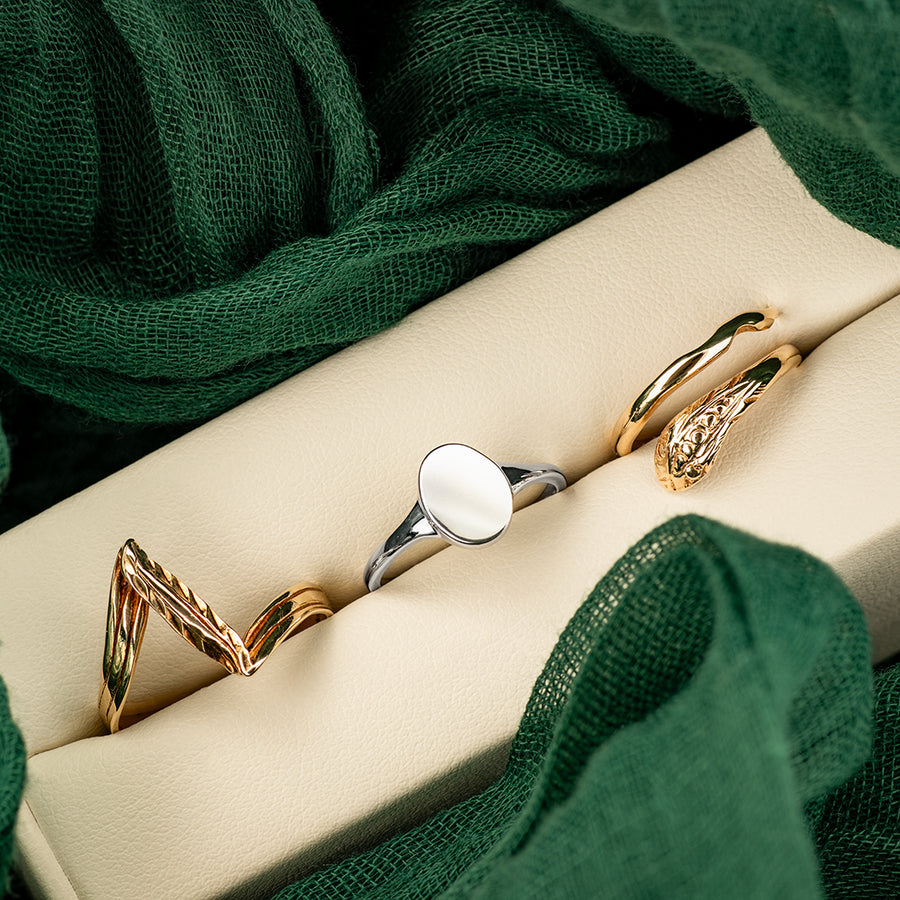 Two gold rings and one silver ring on a beige surface with green fabric in the background
