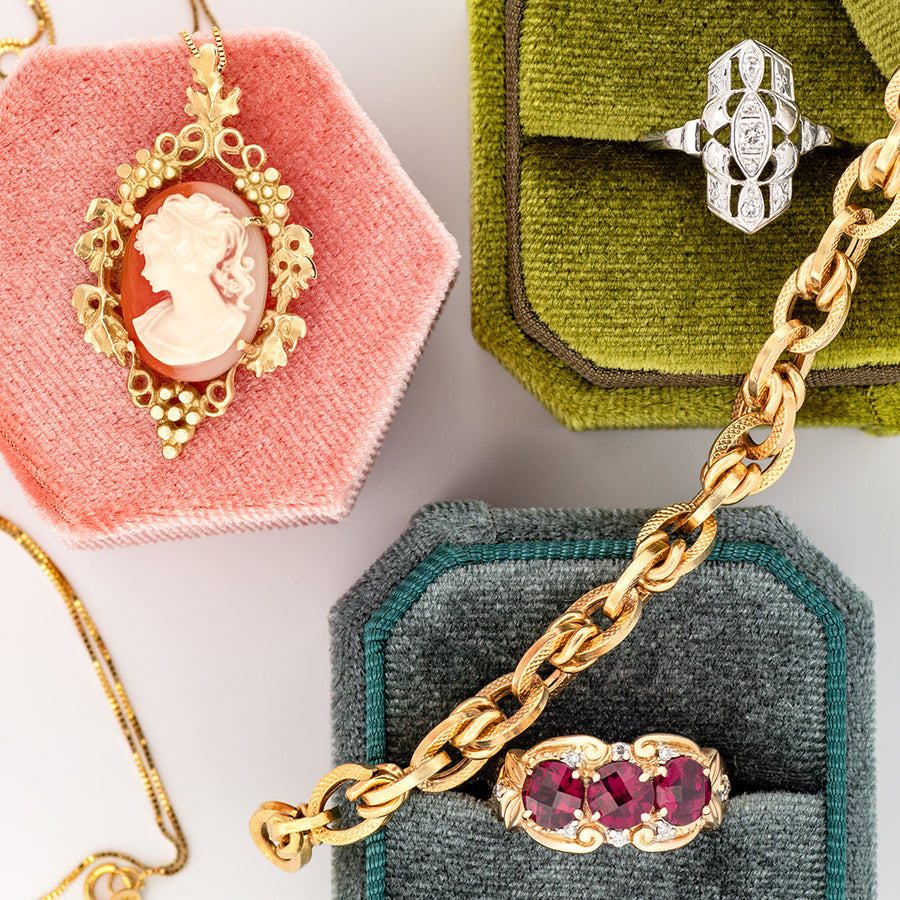 Collection of vintage jewellery in colorful boxes showcasing a gold chain, a red stone ring, a diamond ring and a cameo necklace. 