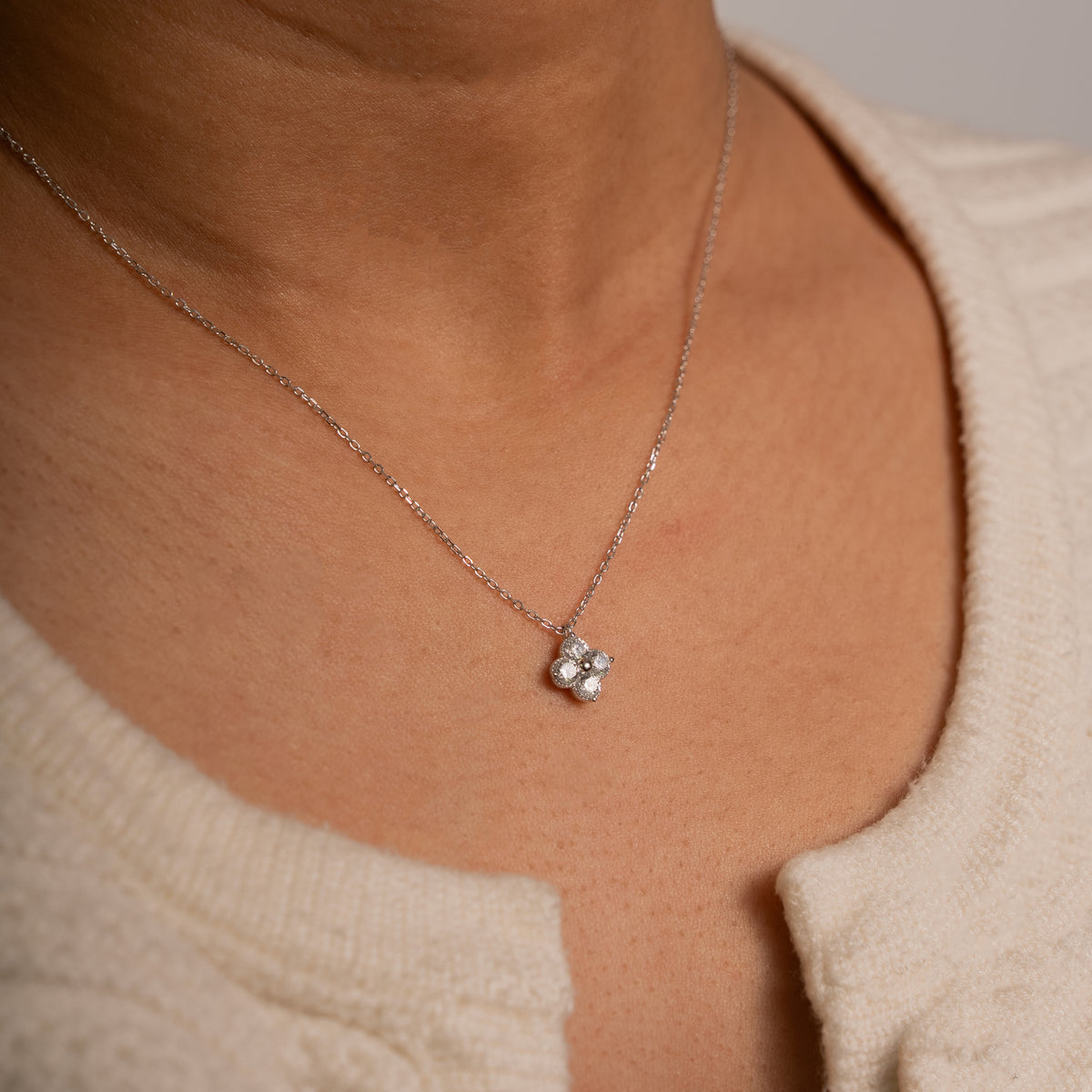 A close-up of a person wearing a delicate silver chain necklace with a small four-stone pendant.