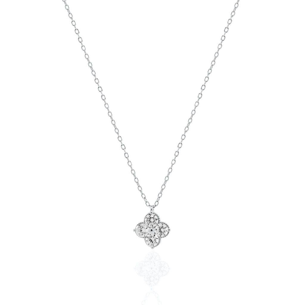 A delicate silver chain necklace with a small four-petal flower pendant set with clear stones, displayed on a clean white background with a soft reflection below.