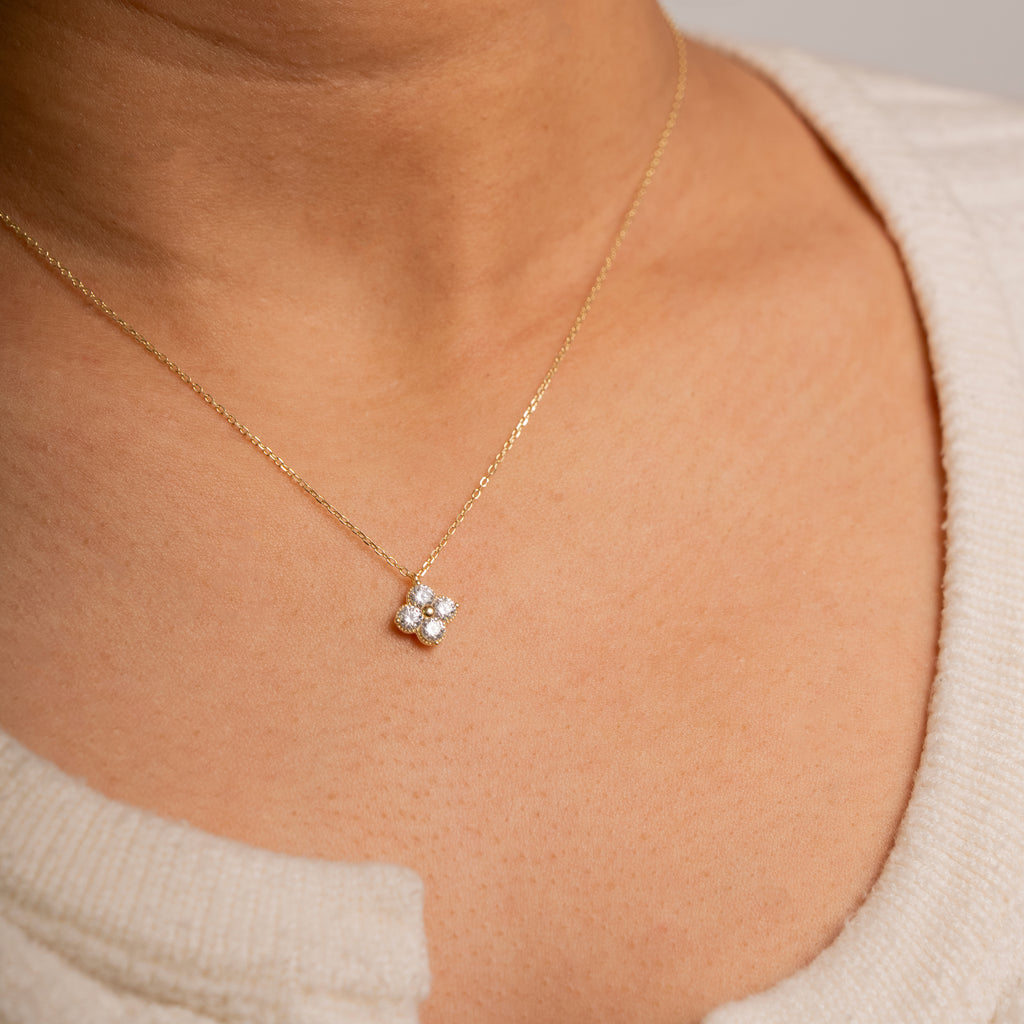 A close-up of a person's neck and chest wearing a delicate yellow gold chain necklace with a small four-stone pendant.