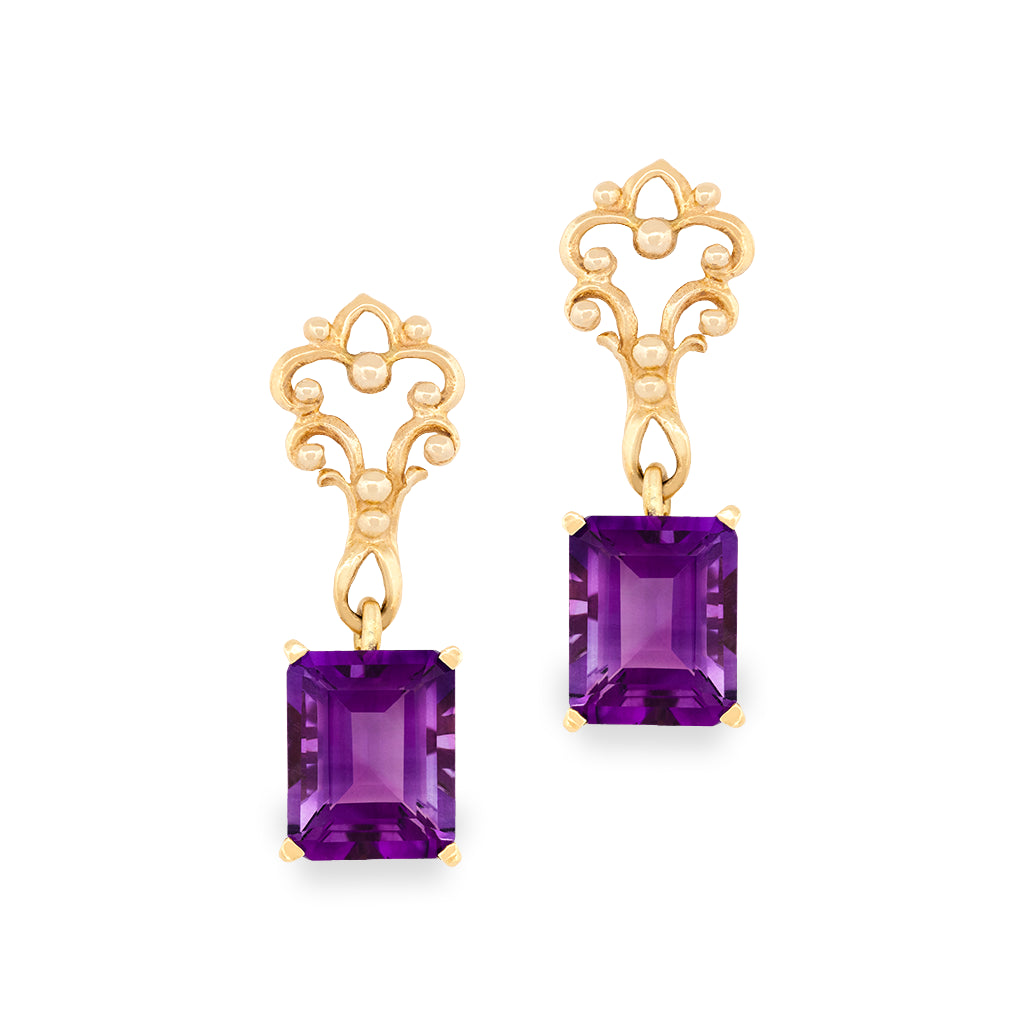 A pair of gold drop earrings featuring rectangular purple amethyst gemstones and ornate gold scrollwork tops, shown on a plain white background.
