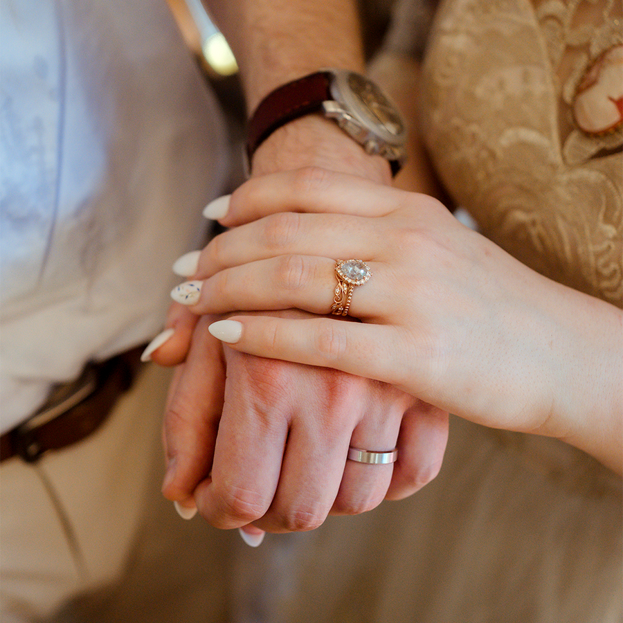 Two hands holding each other, with both hands wearing wedding rings.