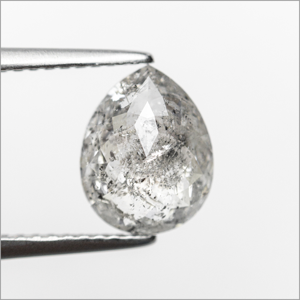 A pear-shaped fancy salt and pepper held between metal tweezers against a plain light gray background.