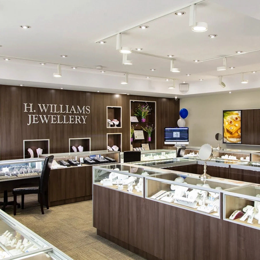 A spacious H. Williams Jewellery retail store interior with multiple glass display cases, wood-look counters, jewelry stands, and ceiling-mounted track lighting.