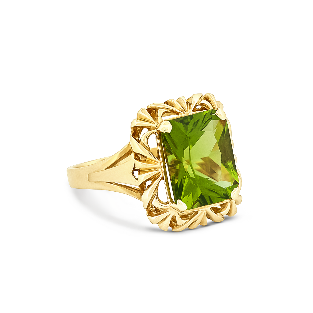 A yellow gold ring featuring a large, cushion-cut green peridot gemstone in an ornate, decorative setting with leaf-like scrollwork, shown on a clean white background.