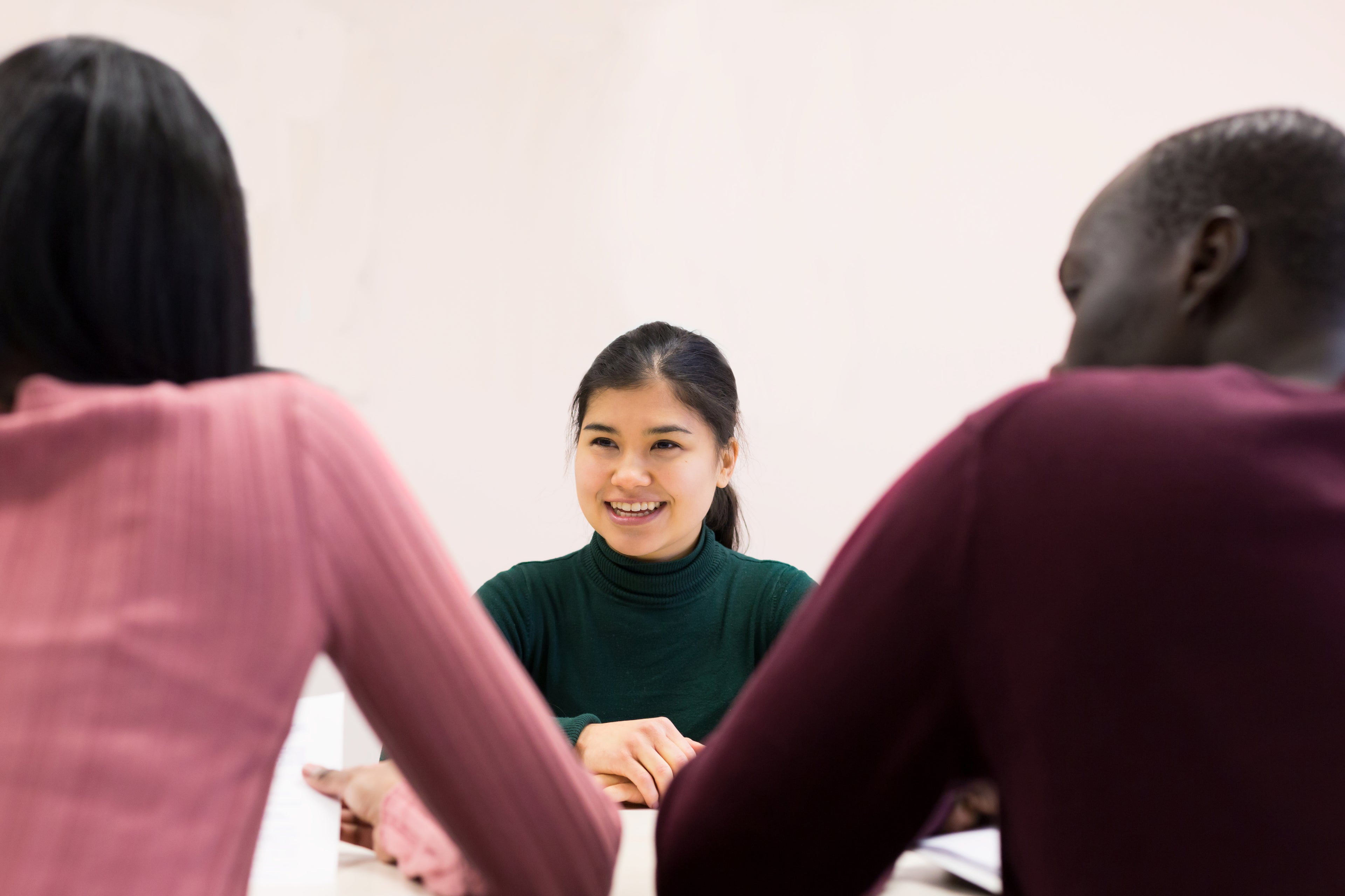 Three people engage in a meeting in front of a white wall. 